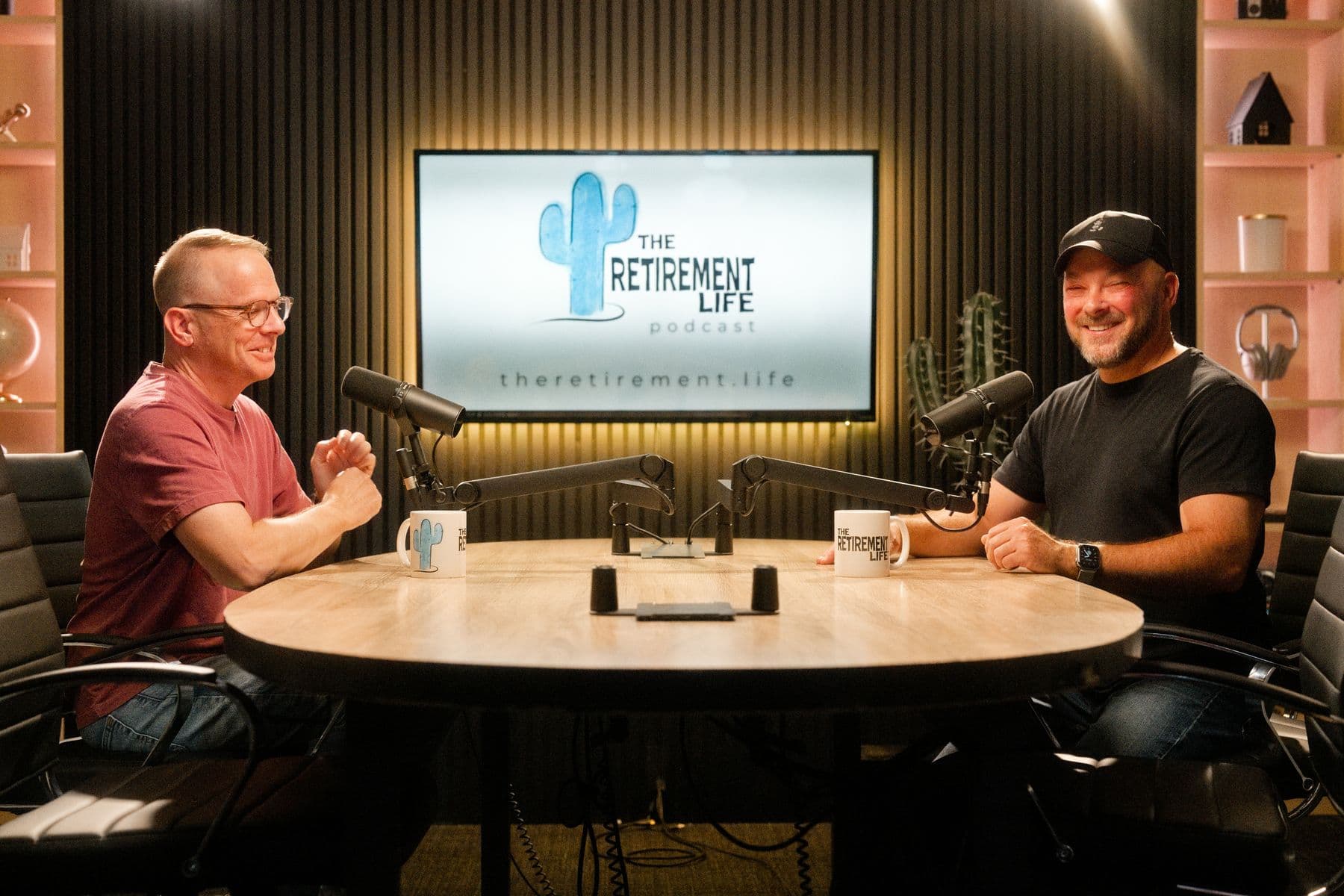 The Retirement Life podcast hosts at the studio table, with the show's logo on the screen behind them.